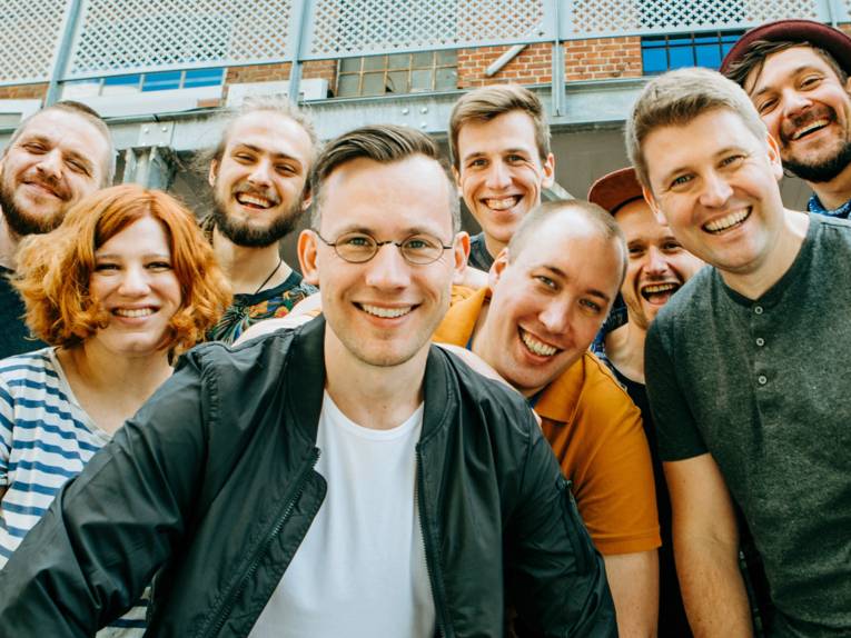 Die zahlreichen Mitglieder der Band Berlin Boom Orchestra lachen in die Kamera.