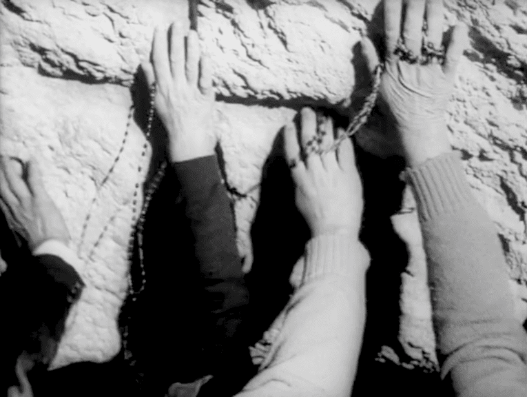 Schwarzweißfoto, auf dem vier Hände mit Gebetsketten an eine Felswand gelehnt zu sehen sind.