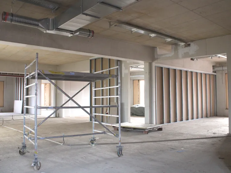 Ein gro&szlig;er Raum im Rohbau, Betonboden, Zwischenw&auml;nden und einem kleinen Ger&uuml;st aus einer Arbeitsebene mit R&auml;dern