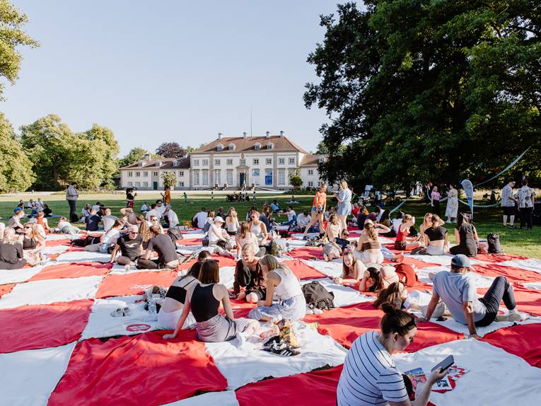 viele Menschen picknicken gemeinsam im Park auf einer großen Decke