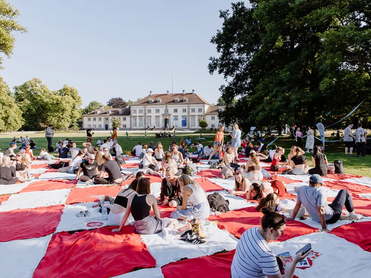 viele Menschen picknicken gemeinsam im Park auf einer großen Decke