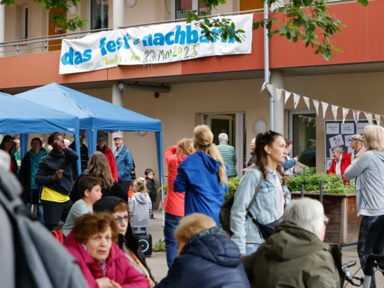 In einem Hof sitzen und stehen Menschen, der Hof ist mit blauen Zelten und F&auml;hnchen gestaltet.