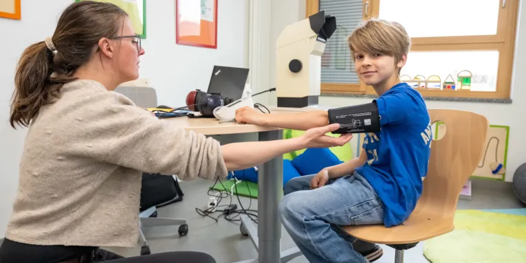 Eine Frau legt einem Jungen die Manschette zum Blutdruck messen an.