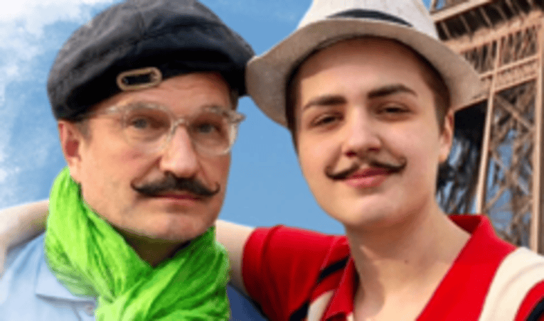 Zwei Menschen vor dem Eiffelturm, in Kostümen, die typisch französisch aussehen.