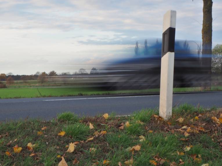 Aufnahme mit Bewegungsunschärfe: Ein Auto fährt auf einer Straße, durch die Bewegung ist das Autor unscharf. Deutlich zu erkennen ist dagegen alles, was sich nicht bewegt.