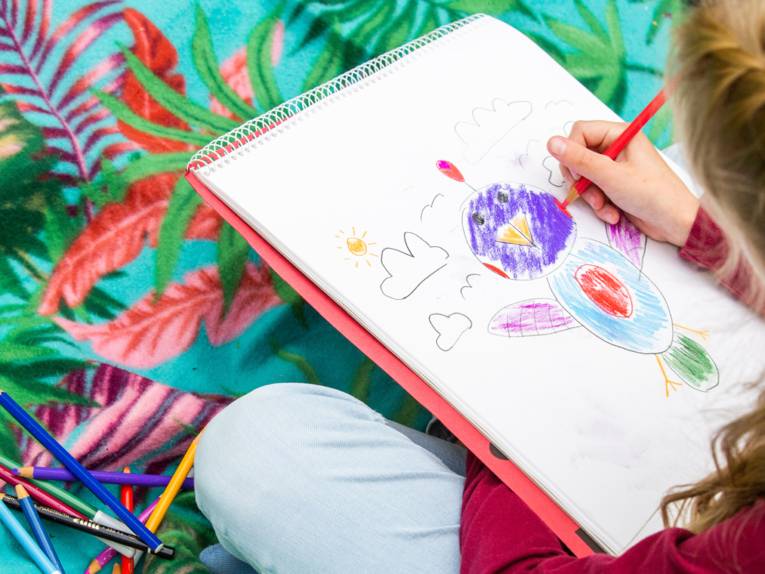 Ein Kind malt auf einem Spiralblock mit Buntstiften.