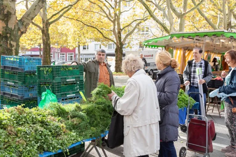 Verk&auml;ufer und Kundschaft an einem Marktstand.