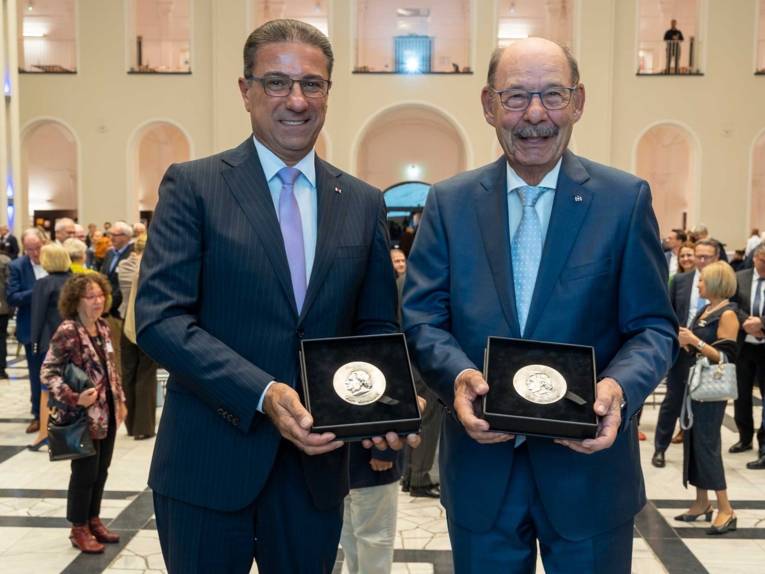 Zwei Männer halten Gedenkmünzen in den Händen.