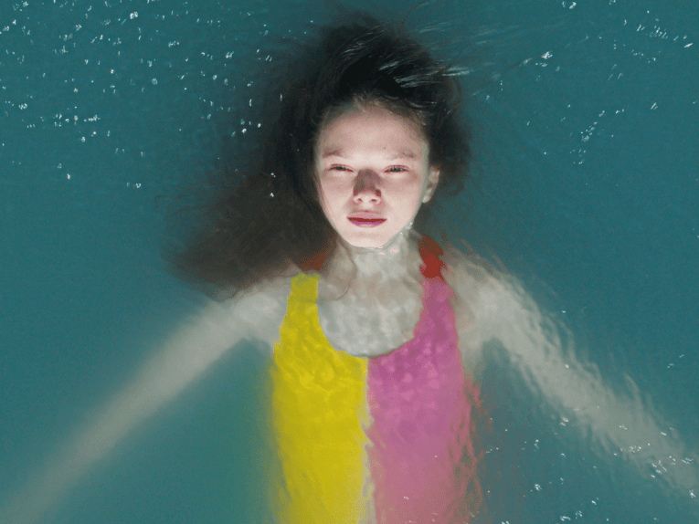 Man sieht von oben auf ein Mädchen, dass auf dem Rücken im Wasser liegt