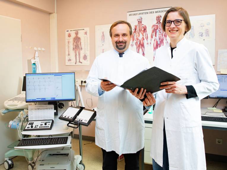 Ein Mann und eine Frau in weißen Kitteln vor medizinischem Diagnosegeräten.