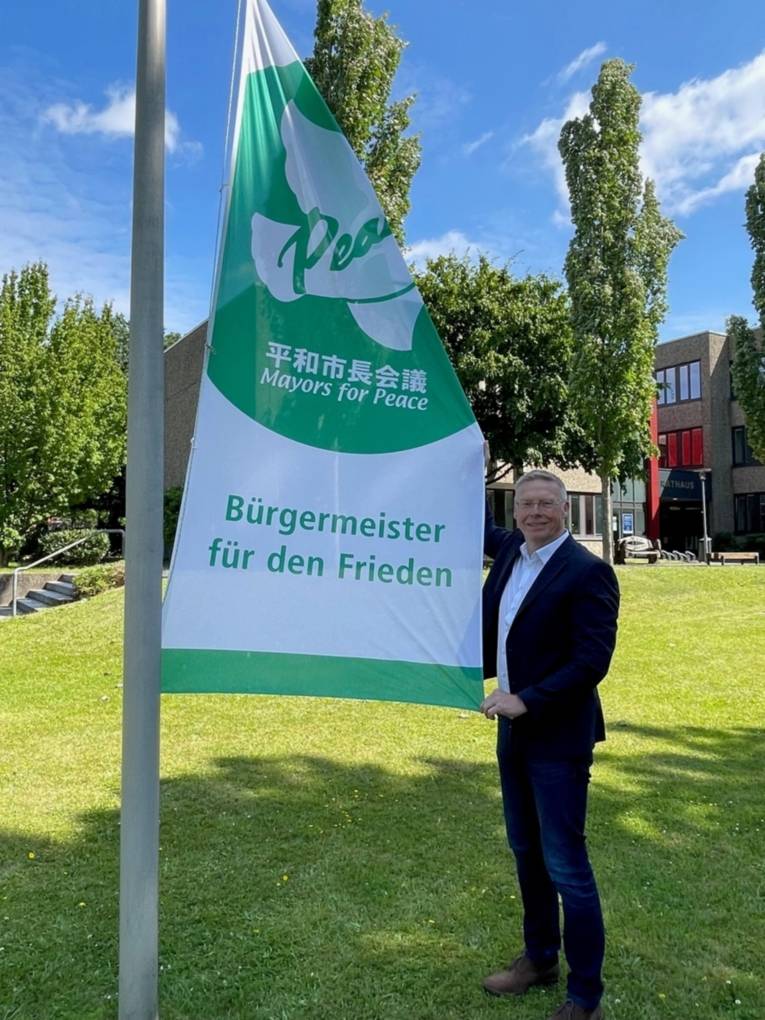 Bürgermeister Andreas Hüffmann präsentiert die Mayors for Peace Flagge vor dem Rathaus der Gemeinde Hiddenhausen
