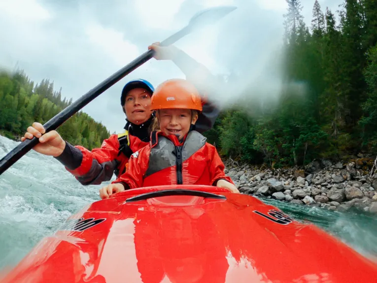 Zu sehen ist eine Frau und ein Kind in einem roten Kayak auf dem Wasser