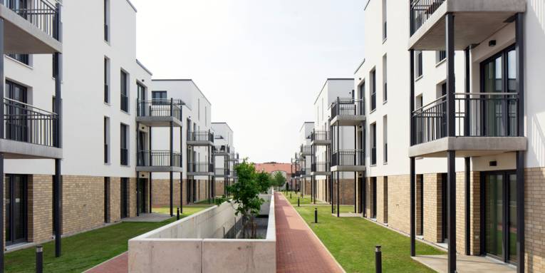 Blick entlang einer Baumpflanzung durch ein Wohnviertel mit einigen modernen Wohngebäuden.