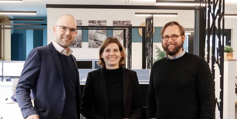 Drei Personen stehen in einer modernen Arbeitsumgebung.