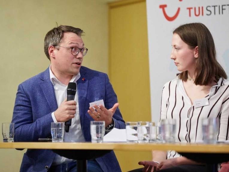 Ein Mann mit Mikro und eine Frau an einem Tisch mit Wassergl&auml;sern