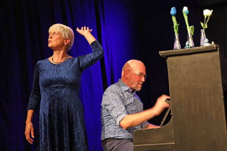 Eine Frau in einem blauen Kleid singt und ein Mann sitzt am Klavier.