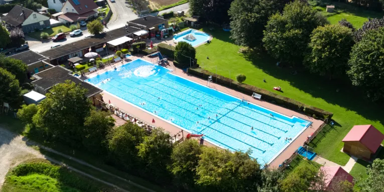 Luftbild vom Freibad mit Schwimmbecken, Kleinkindbecken, Gebäuden und Liegewiese