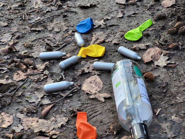 Leere Weinflasche, nicht aufgeblasene Luftballons und CO2-Patronen auf dem Boden liegend.