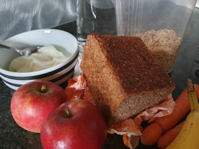 Bild von Brot, Haferflocken, Äpfel, Banane, Joghurt in Müslischale, Möhren, Wasserkaraffe