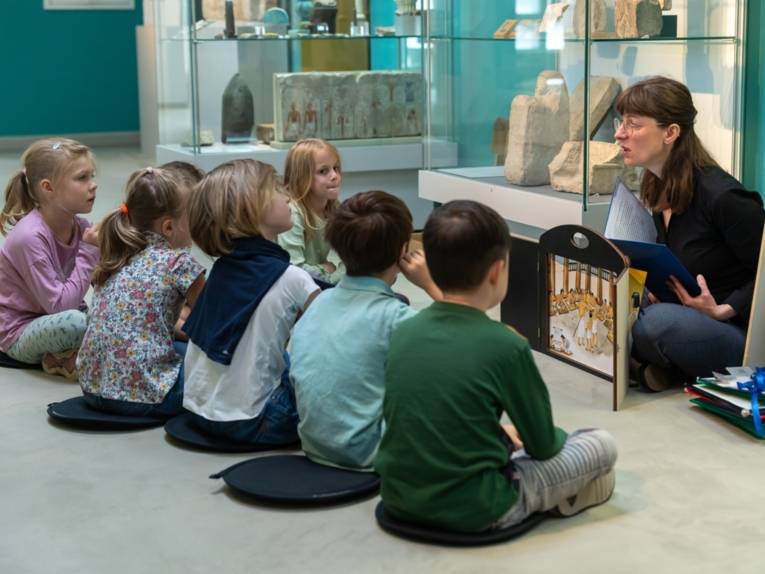 Kinder sitzen im Halbkreis und hören bei einem Programm in der Ägyptischen Sammlung zu