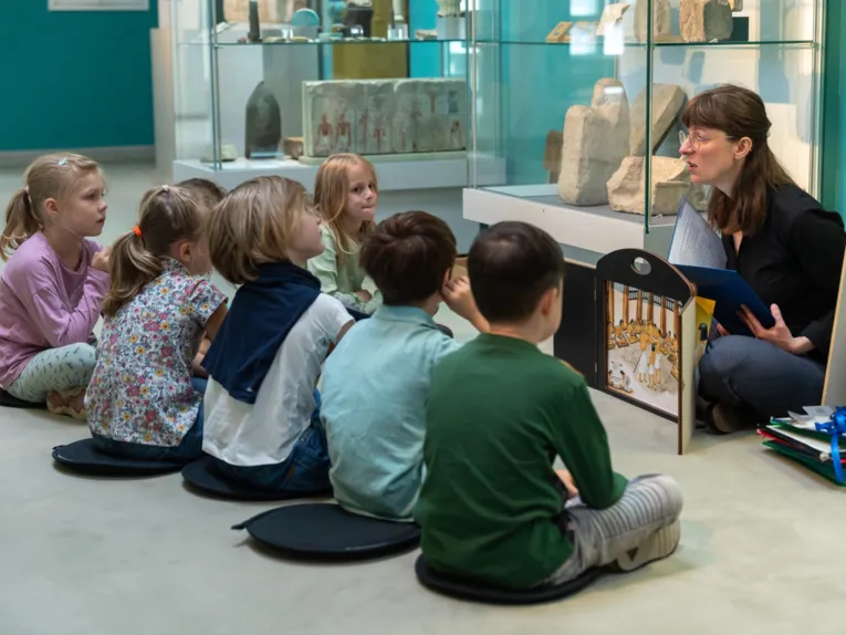 Kinder sitzen im Halbkreis und hören bei einem Programm in der Ägyptischen Sammlung zu