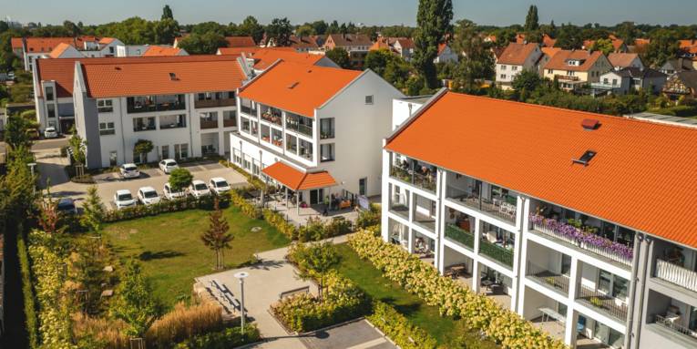 Blick auf mehrere neu gebaute Mehrfamilienhäuser mit roten Dachziegeln, Balkonen und Parkplätzen.