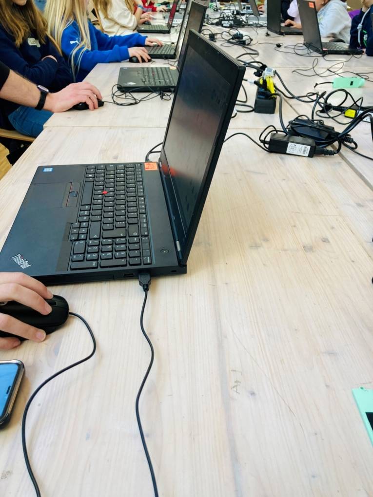 Ein Tisch auf dem ein Laptop steht. Daran arbeitet ein Kind. Drumherum sind viele Kabel.