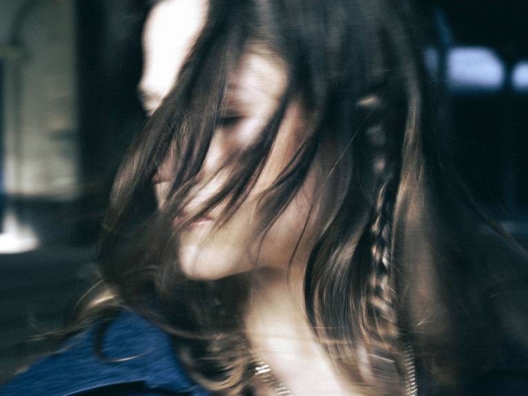 Unscharfes Porträt einer Frau, ein Teil ihres Gesichts ist von ihrem Haar verdeckt.