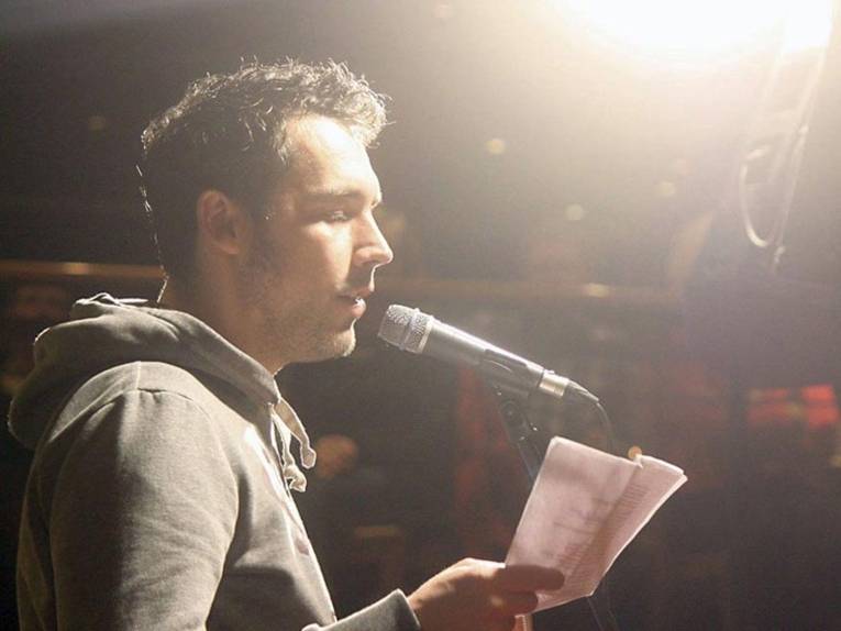 Mann vor einem Mikrofon liest von einem Zettel ab