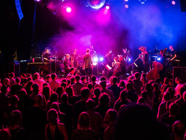 Orchester auf der Bühne vor stehendem Publikum.
