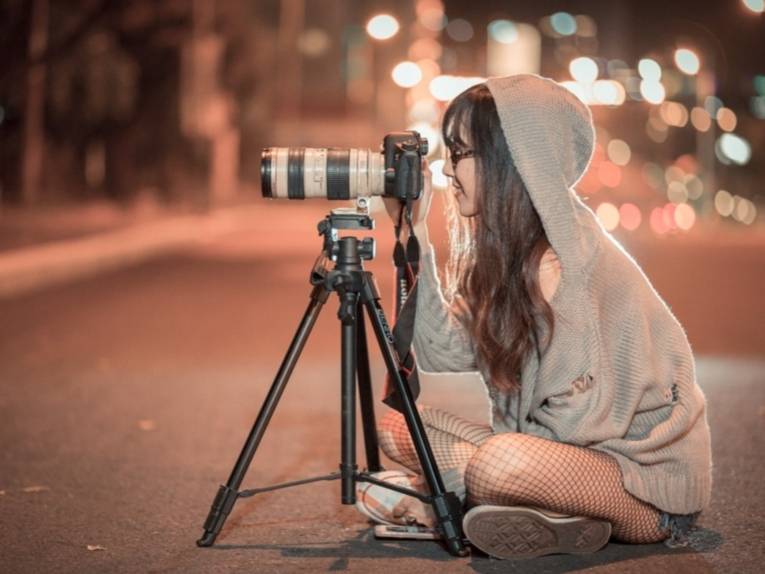 Eine junge Frau sitzt mit einer Kamera auf einem Stativ auf einer Straße