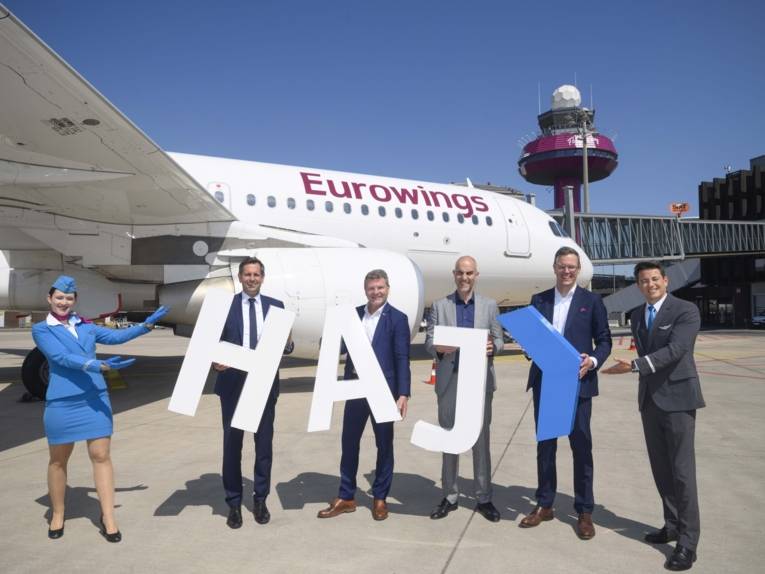 Vier Männer in Anzügen und eine Flugbegleiterin stehen vor einem Eurowings-Flugzeug.