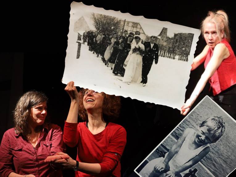 Drei Frauen mit zwei großen Fotos von einer Hochzeitsgesellschaft und einem Kind