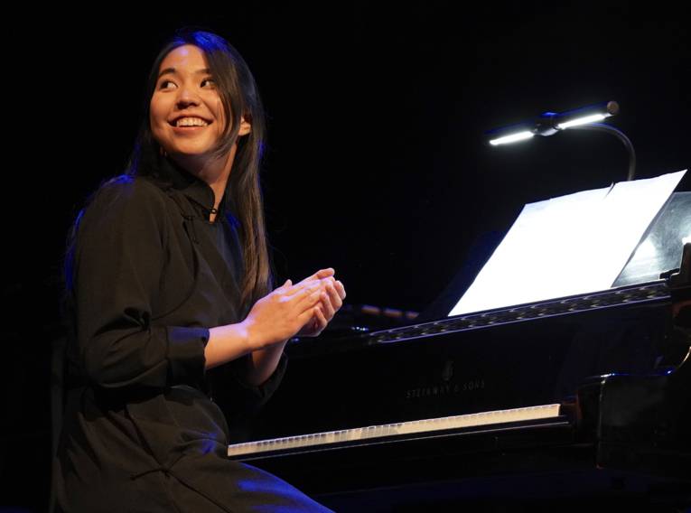Lachende Frau mit langem Haar sitzt an einem Klavier.