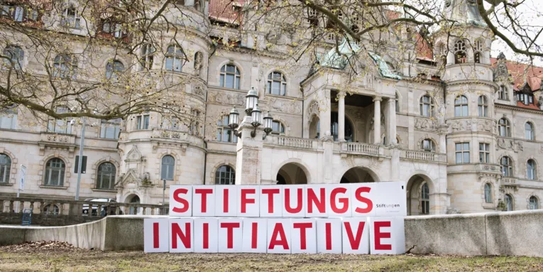 Kartons mit Buchstaben, die das Wort Stiftungsinitiative ergeben, vor einem historischen Gebäude
