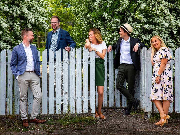 Die zwei Sängerinnen und drei Sänger des Ensembles stehen an einem Gartenzaun.