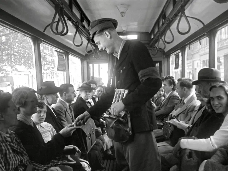Schwarz-Wei&szlig;-Fotografie: Ein Mann tr&auml;gt eine Dienstm&uuml;tze und verkauft Fahrscheine gegen Bargeld in einer Stra&szlig;enbahn.