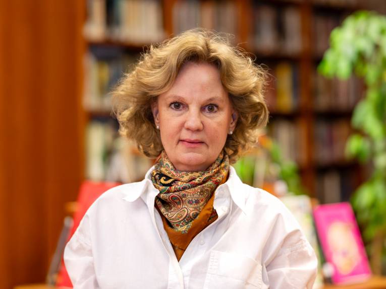 Portraitfotografie einer Frau mit einem verschwommenen Bücherregal im Hintergrund.