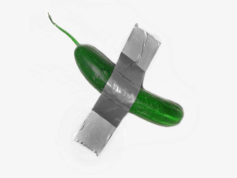 Eine Gurke hängt mit einem Klebeband befestigt an einer Wand