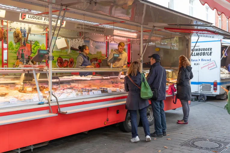 Kundschaft und Verkaufspersonal an einem Fleischerei-Wagen.