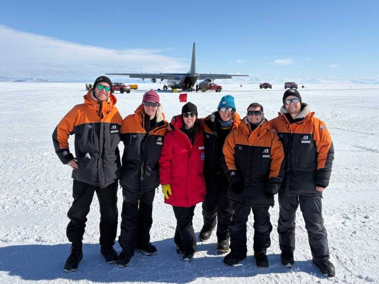 Menschen auf arktischem Eis, im Hintergrund ein Transportflugzeug