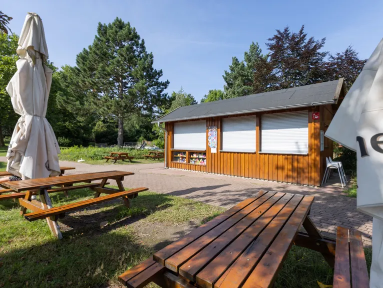 Holzb&auml;nke und Tische, zusammengeklappte Sonnenschirme, im Hintergrund ein Kiosk mit Holzw&auml;nden