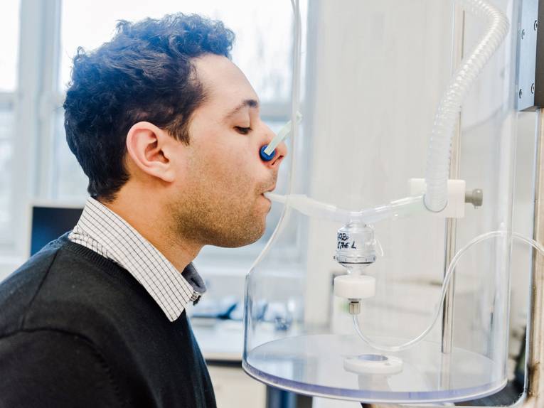 Ein Mann mit Nasenklammer und einem Mundstück in seinem Mund, das an einem Glasbehälter angebracht ist.