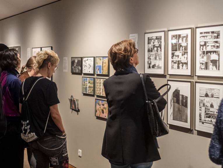 Besuchende schauen auf an Wänden aufgehängte Karikaturen und Comicseiten.