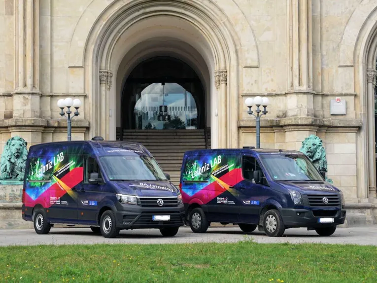 Zwei Transporter mit der Aufschrift "LeibnizLAB" vor dem Portal eines historischen Gebäudes.