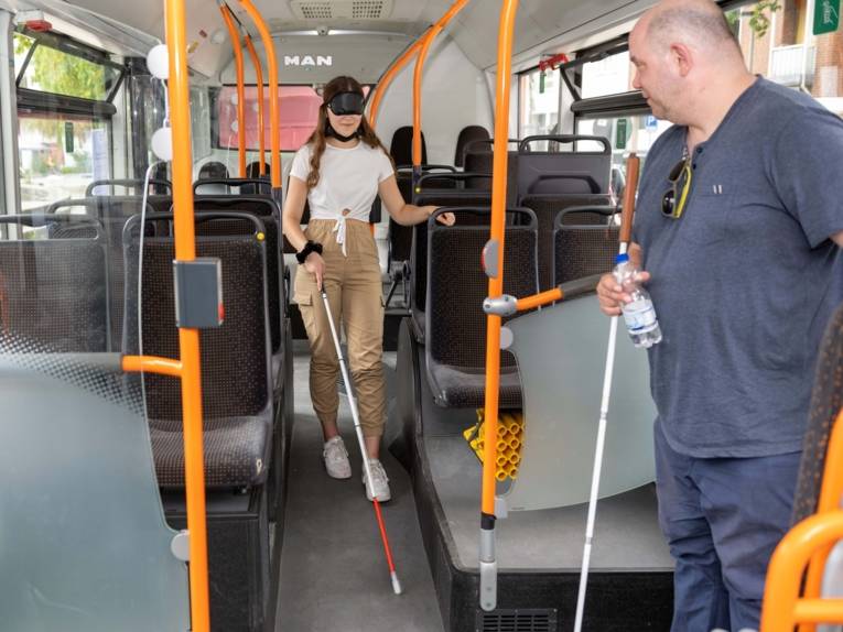 Ein Mädchen mit einer Augenbinde und Blindenstock in einem Bus. Sie nimmt an einem Experiment teil, um zu erfahren wie es sich anfühlt blind in einem Bus zu fahren