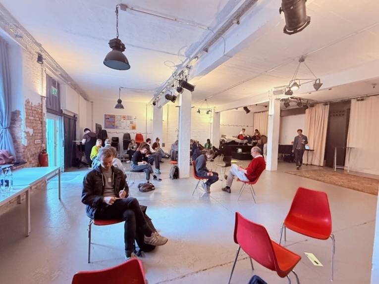 Die Workshopteilnehmer:innen sitzen auf Stühlen im Raum verteilt und schreiben für sich.