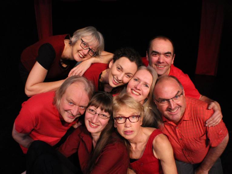 Fünf Frauen und drei Männer in roter Kleidung lächeln in die Kamera.