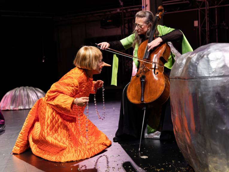 Pinocchio kniet vor einer Cello-Spielerin.