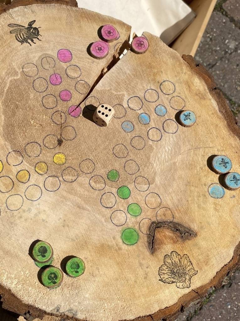 Auf eine Baumscheibe ist das Spielbrett eines W&uuml;rfelspiels gezeichnet. Felder sind farbig markiert und Stempel verzieren das Spielbrett.